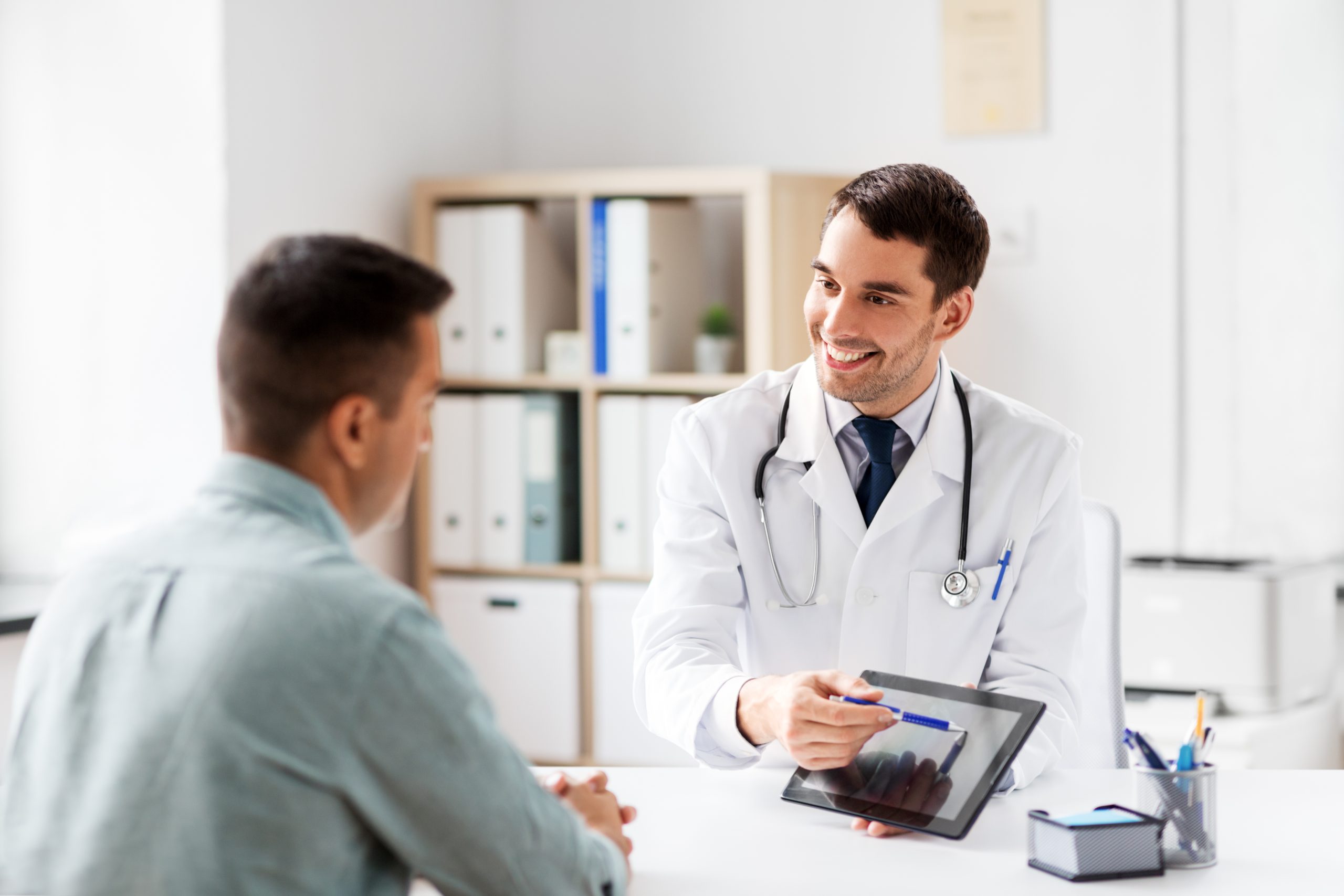 medicine, healthcare and technology concept - doctor with tablet pc computer and male patient talking at medical office in hospital; Shutterstock ID 1238588452; purchase_order: Limited 7/26/21