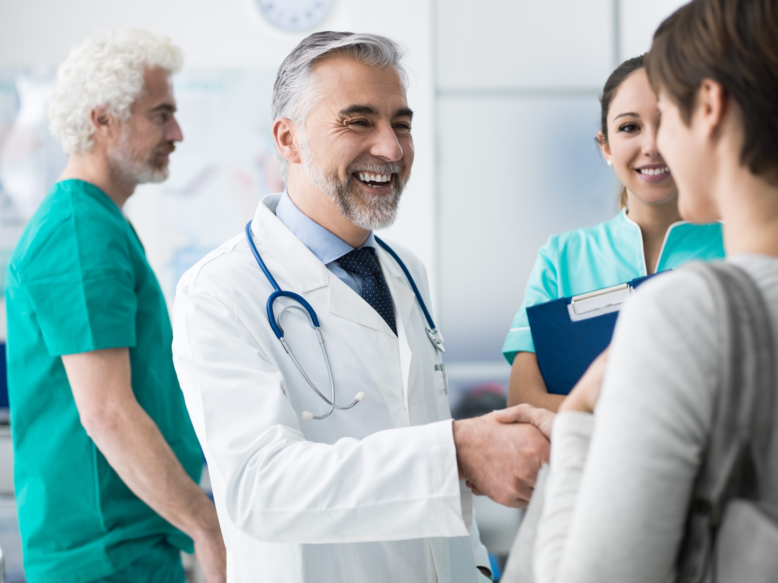 Smiling confident doctor shaking patients hand at the hospital and medical team ; Shutterstock ID 767125756; Purchase Order: comps; Job: ; Client/Licensee: ; Other: